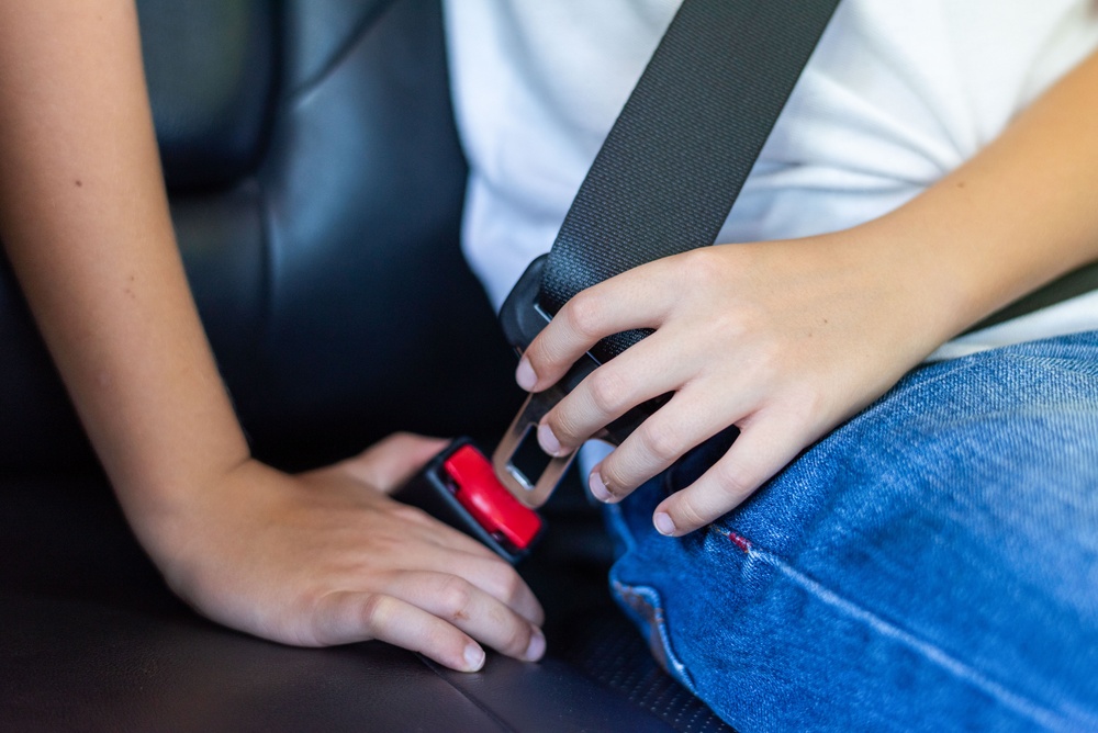 Close-up of a child fastening a seatbelt while sitting in a car.
